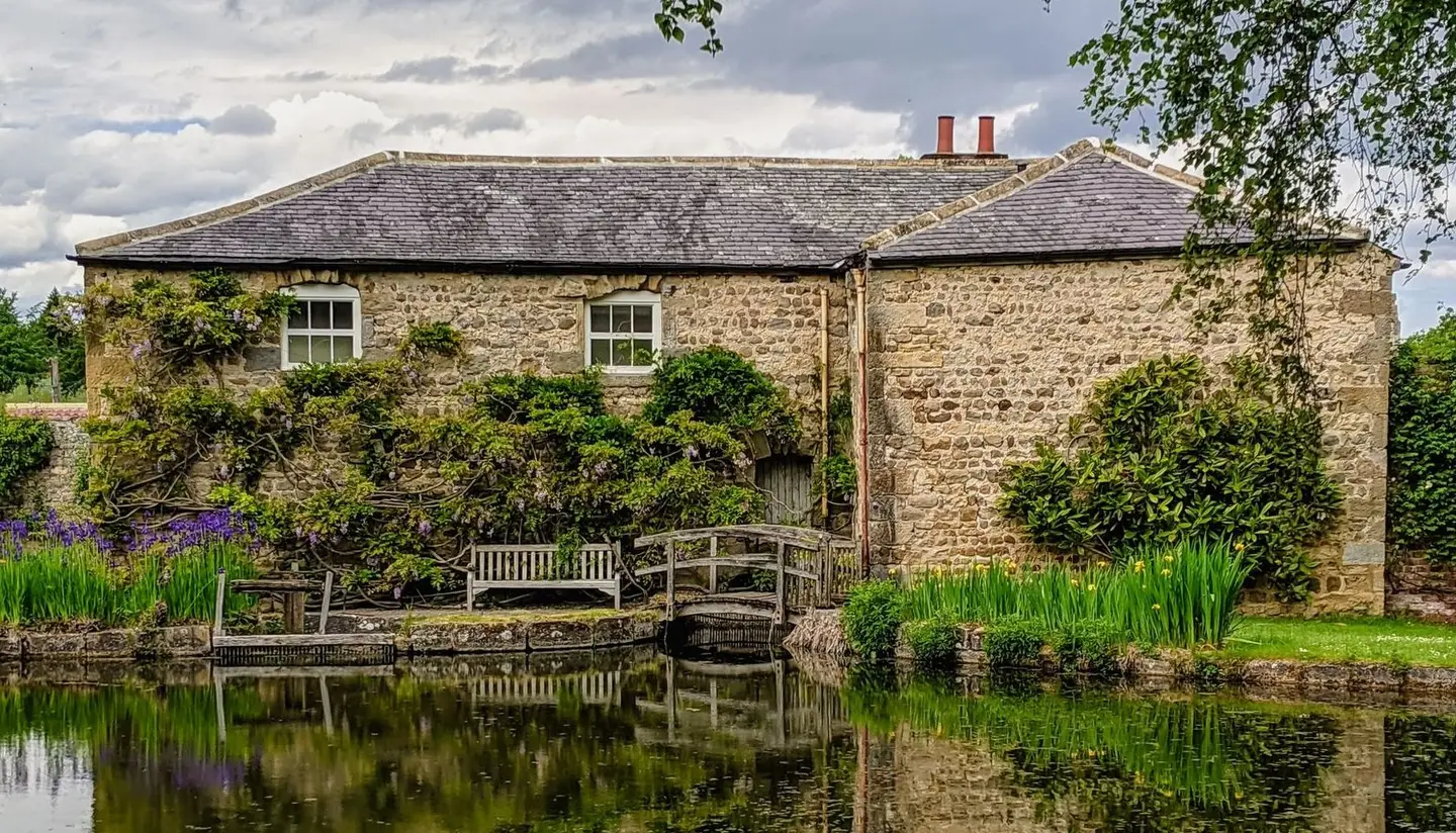 Historic stone building reflected in a calm pond in North Stainley, England