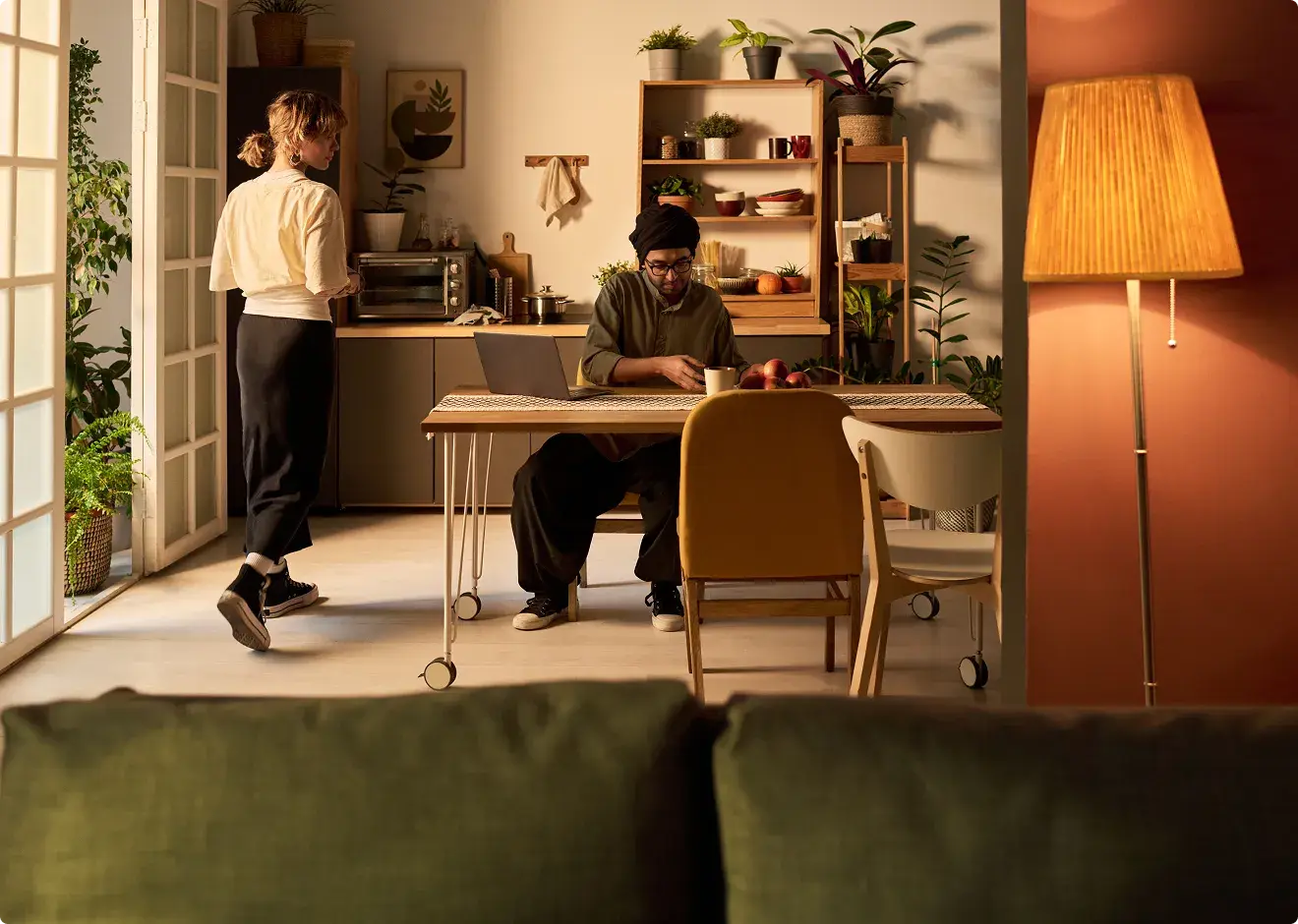 A couple at home in a warm, plant-filled kitchen